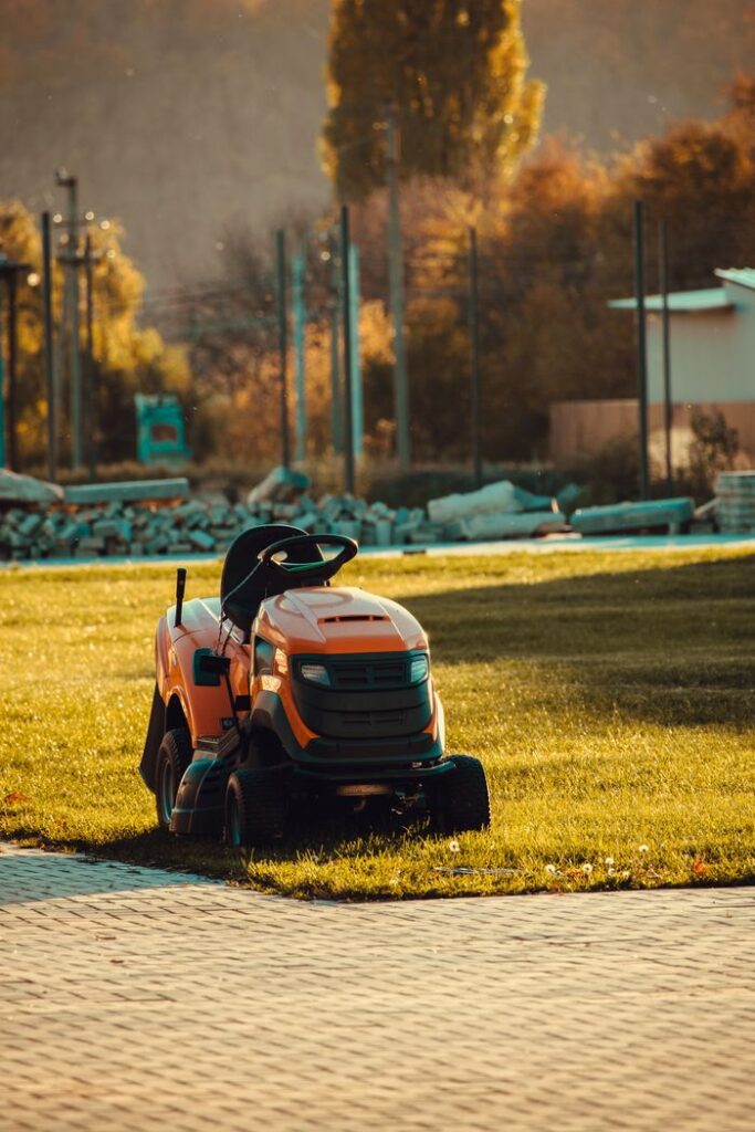 Vibrant orange lawn mower parked on a sunlit lawn during a beautiful autumn afternoon.